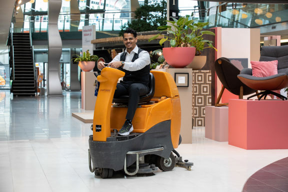 Schoonmaakmedewerker die vloeren aan het schoonmaken is op een schrobmachine