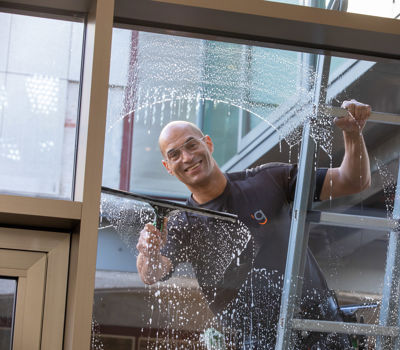 Glazenwasser die op een ladder ramen staat te lappen van een bedrijfspand
